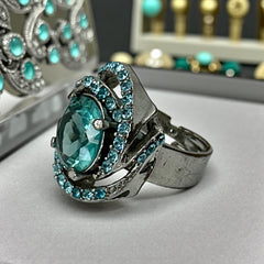 Adjustable silver-tone cocktail ring with a large round aqua rhinestone cabochon and open swirl design set with smaller teal rhinestones; vintage-inspired statement jewelry in very good condition.