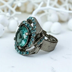 Adjustable silver-tone cocktail ring with a large round aqua rhinestone cabochon and open swirl design set with smaller teal rhinestones; vintage-inspired statement jewelry in very good condition.
