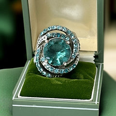 Adjustable silver-tone cocktail ring with a large round aqua rhinestone cabochon and open swirl design set with smaller teal rhinestones; vintage-inspired statement jewelry in very good condition.