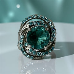 Adjustable silver-tone cocktail ring with a large round aqua rhinestone cabochon and open swirl design set with smaller teal rhinestones; vintage-inspired statement jewelry in very good condition.