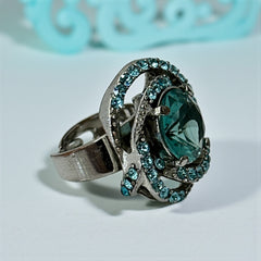 Adjustable silver-tone cocktail ring with a large round aqua rhinestone cabochon and open swirl design set with smaller teal rhinestones; vintage-inspired statement jewelry in very good condition.