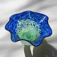 Signed BAGI art glass bowl with a footed base and wavy rim, featuring mottled blue and green swirls. The glass has a glossy finish and sculptural form, with vibrant oceanic and forest tones. Dimensions approximately 5–5½" tall and 7–8" wide.