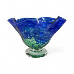 Signed BAGI art glass bowl with a footed base and wavy rim, featuring mottled blue and green swirls. The glass has a glossy finish and sculptural form, with vibrant oceanic and forest tones. Dimensions approximately 5–5½" tall and 7–8" wide.