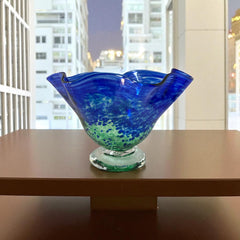 Signed BAGI art glass bowl with a footed base and wavy rim, featuring mottled blue and green swirls. The glass has a glossy finish and sculptural form, with vibrant oceanic and forest tones. Dimensions approximately 5–5½" tall and 7–8" wide.