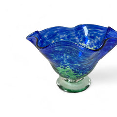 Signed BAGI art glass bowl with a footed base and wavy rim, featuring mottled blue and green swirls. The glass has a glossy finish and sculptural form, with vibrant oceanic and forest tones. Dimensions approximately 5–5½" tall and 7–8" wide.