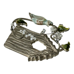 Vintage 1990s silver tone brooch featuring a light blue enamel bird perched on a wire branch with green enamel leaves and white seed bead flowers, set in front of a textured birdhouse; whimsical 3D design in very good vintage condition.