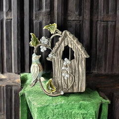 Vintage 1990s silver tone brooch featuring a light blue enamel bird perched on a wire branch with green enamel leaves and white seed bead flowers, set in front of a textured birdhouse; whimsical 3D design in very good vintage condition.