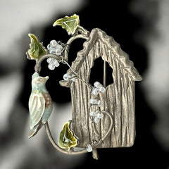 Vintage 1990s silver tone brooch featuring a light blue enamel bird perched on a wire branch with green enamel leaves and white seed bead flowers, set in front of a textured birdhouse; whimsical 3D design in very good vintage condition.