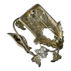 Vintage 1990s silver tone brooch featuring a light blue enamel bird perched on a wire branch with green enamel leaves and white seed bead flowers, set in front of a textured birdhouse; whimsical 3D design in very good vintage condition.