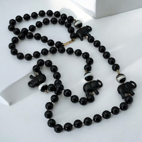 Vintage 1990s necklace featuring a symmetrical design with two elephant-shaped black beads, two black-and-white beads resembling banded agate, and a strand of 8mm black plastic beads in very good condition
