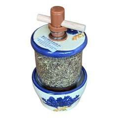 Provence ceramic herb mill with hand-painted blue lavender sprigs and green leaves on a cream base, featuring a glass chamber filled with dried herbs and a wooden crossbar handle for grinding.
