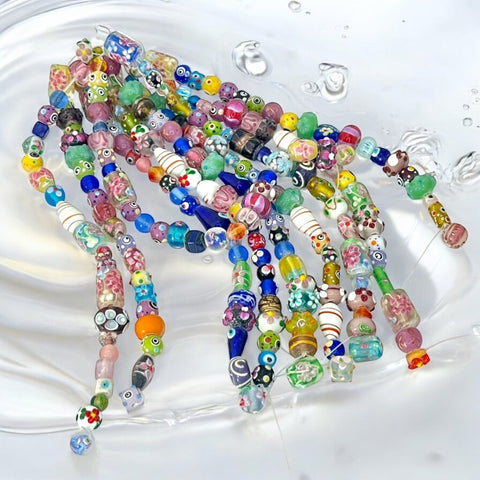 A strand of vintage Chinese lampwork beads from the 1990s, featuring colorful floral and geometric designs in various shapes like oval, cube, and round tube. Each strand includes approximately 20 unique glass beads, new old stock, with a vibrant and playful aesthetic.