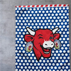 Coucke tea towel featuring a modern design of the red laughing cow with cheese box earrings on a blue background with white polka dots. Made of 100% cotton, blending playful charm with French culinary heritage.