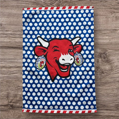 Coucke tea towel featuring a modern design of the red laughing cow with cheese box earrings on a blue background with white polka dots. Made of 100% cotton, blending playful charm with French culinary heritage.
