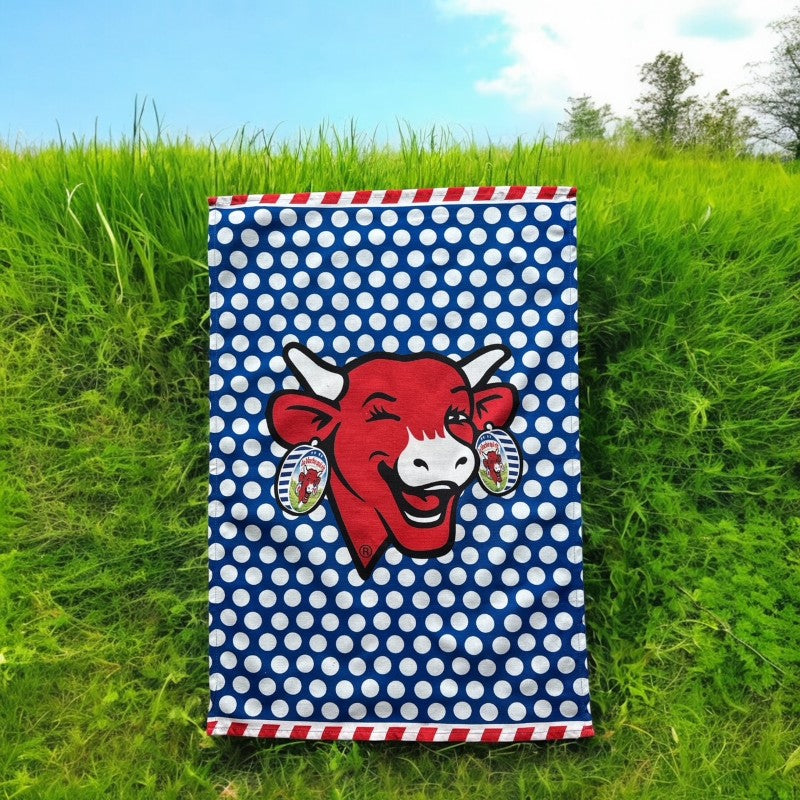 Coucke tea towel featuring a modern design of the red laughing cow with cheese box earrings on a blue background with white polka dots. Made of 100% cotton, blending playful charm with French culinary heritage.