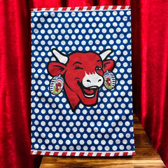 Coucke tea towel featuring a modern design of the red laughing cow with cheese box earrings on a blue background with white polka dots. Made of 100% cotton, blending playful charm with French culinary heritage.