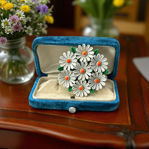 Vintage 1960s enamel daisy brooch with white petals, orange centers, and green leaves in a round floral cluster. Silver-toned finish, 2-inch diameter, in very good condition.
