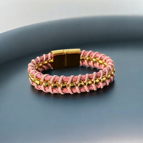 Elegant Daniel Steiger Melrose bracelet featuring braided pink leather on each side of yellow gold-plated center links, finished with a gold-plated magnetic slide clasp, photographed against a neutral backdrop.