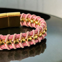 Elegant Daniel Steiger Melrose bracelet featuring braided pink leather on each side of yellow gold-plated center links, finished with a gold-plated magnetic slide clasp, photographed against a neutral backdrop.