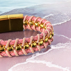 Elegant Daniel Steiger Melrose bracelet featuring braided pink leather on each side of yellow gold-plated center links, finished with a gold-plated magnetic slide clasp, photographed against a neutral backdrop.