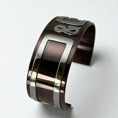 Dolce & Gabbana men's stainless steel cuff bracelet with a brown finish and raised silver-tone logo plaque; modern designer accessory with bold branding and sculptural detail.