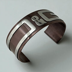 Dolce & Gabbana men's stainless steel cuff bracelet with a brown finish and raised silver-tone logo plaque; modern designer accessory with bold branding and sculptural detail.
