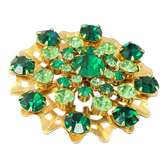 Vintage 1950s gold tone brooch with a ruffled sunburst design, featuring concentric rings of emerald and peridot rhinestones and a large green center stone; bold mid-century costume jewelry with layered sparkle and sculptural detail.
