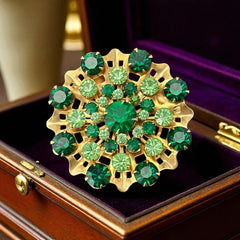 Vintage 1950s gold tone brooch with a ruffled sunburst design, featuring concentric rings of emerald and peridot rhinestones and a large green center stone; bold mid-century costume jewelry with layered sparkle and sculptural detail.
