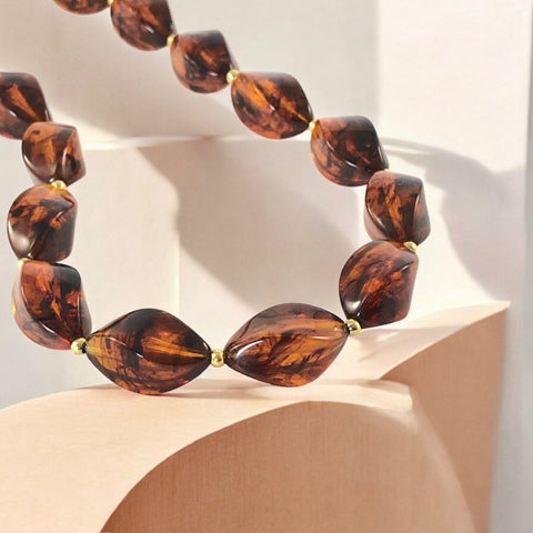 1950s vintage faux amber necklace featuring cognac-colored twisted plastic beads with gold-tone accents and a matching barrel clasp. A shiny, elegant piece in very good vintage condition, perfect for sustainable and eco-conscious fashion.