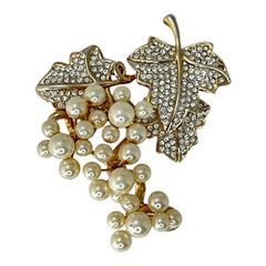 Elegant vintage 1980s brooch featuring a gold-tone grape vine design with round faux pearls forming the grape cluster. The leaves are adorned with sparkling clear pave rhinestones, adding a luxurious touch. Unsigned and in very good vintage condition, this brooch is a timeless statement piece.