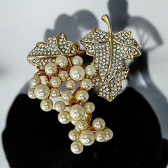 Elegant vintage 1980s brooch featuring a gold-tone grape vine design with round faux pearls forming the grape cluster. The leaves are adorned with sparkling clear pave rhinestones, adding a luxurious touch. Unsigned and in very good vintage condition, this brooch is a timeless statement piece.