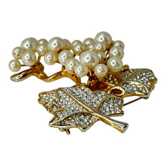 Elegant vintage 1980s brooch featuring a gold-tone grape vine design with round faux pearls forming the grape cluster. The leaves are adorned with sparkling clear pave rhinestones, adding a luxurious touch. Unsigned and in very good vintage condition, this brooch is a timeless statement piece.