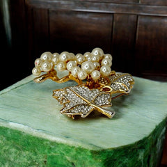 Elegant vintage 1980s brooch featuring a gold-tone grape vine design with round faux pearls forming the grape cluster. The leaves are adorned with sparkling clear pave rhinestones, adding a luxurious touch. Unsigned and in very good vintage condition, this brooch is a timeless statement piece.