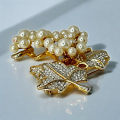 Elegant vintage 1980s brooch featuring a gold-tone grape vine design with round faux pearls forming the grape cluster. The leaves are adorned with sparkling clear pave rhinestones, adding a luxurious touch. Unsigned and in very good vintage condition, this brooch is a timeless statement piece.