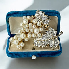 Elegant vintage 1980s brooch featuring a gold-tone grape vine design with round faux pearls forming the grape cluster. The leaves are adorned with sparkling clear pave rhinestones, adding a luxurious touch. Unsigned and in very good vintage condition, this brooch is a timeless statement piece.