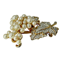 Elegant vintage 1980s brooch featuring a gold-tone grape vine design with round faux pearls forming the grape cluster. The leaves are adorned with sparkling clear pave rhinestones, adding a luxurious touch. Unsigned and in very good vintage condition, this brooch is a timeless statement piece.