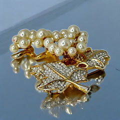 Elegant vintage 1980s brooch featuring a gold-tone grape vine design with round faux pearls forming the grape cluster. The leaves are adorned with sparkling clear pave rhinestones, adding a luxurious touch. Unsigned and in very good vintage condition, this brooch is a timeless statement piece.