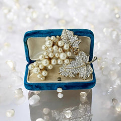 Elegant vintage 1980s brooch featuring a gold-tone grape vine design with round faux pearls forming the grape cluster. The leaves are adorned with sparkling clear pave rhinestones, adding a luxurious touch. Unsigned and in very good vintage condition, this brooch is a timeless statement piece.