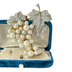 Elegant vintage 1980s brooch featuring a gold-tone grape vine design with round faux pearls forming the grape cluster. The leaves are adorned with sparkling clear pave rhinestones, adding a luxurious touch. Unsigned and in very good vintage condition, this brooch is a timeless statement piece.