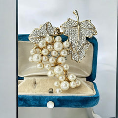 Elegant vintage 1980s brooch featuring a gold-tone grape vine design with round faux pearls forming the grape cluster. The leaves are adorned with sparkling clear pave rhinestones, adding a luxurious touch. Unsigned and in very good vintage condition, this brooch is a timeless statement piece.