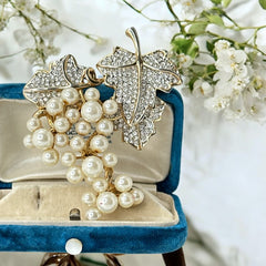 Elegant vintage 1980s brooch featuring a gold-tone grape vine design with round faux pearls forming the grape cluster. The leaves are adorned with sparkling clear pave rhinestones, adding a luxurious touch. Unsigned and in very good vintage condition, this brooch is a timeless statement piece.
