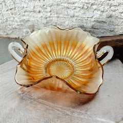 Vintage Fenton marigold carnival glass dish with stippled rays pattern, featuring a ruffled scalloped edge and clear double handles; warm amber iridescence with visible air bubbles