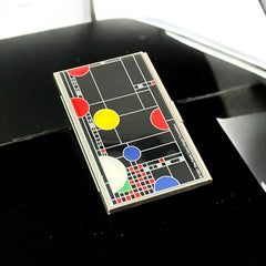 Acme Studio business/credit card case featuring Frank Lloyd Wright's 'Playhouse' design, showcasing geometric patterns with red, yellow, and blue accents on a black background, crafted with mirror chrome metal finish and lacquer-filled acid-etched image.