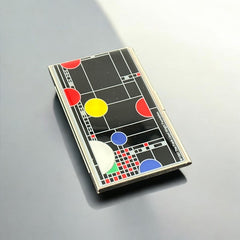 Acme Studio business/credit card case featuring Frank Lloyd Wright's 'Playhouse' design, showcasing geometric patterns with red, yellow, and blue accents on a black background, crafted with mirror chrome metal finish and lacquer-filled acid-etched image.