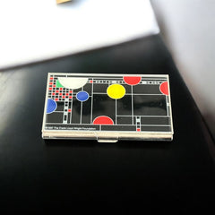 Acme Studio business/credit card case featuring Frank Lloyd Wright's 'Playhouse' design, showcasing geometric patterns with red, yellow, and blue accents on a black background, crafted with mirror chrome metal finish and lacquer-filled acid-etched image.