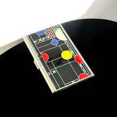 Acme Studio business/credit card case featuring Frank Lloyd Wright's 'Playhouse' design, showcasing geometric patterns with red, yellow, and blue accents on a black background, crafted with mirror chrome metal finish and lacquer-filled acid-etched image.