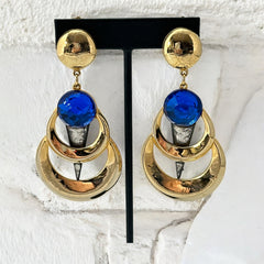 Vintage French modernist clip-on earrings with faceted blue round cabochons, layered gold and silver-tone metal crescents, and long sculptural dangles; shown from multiple angles to highlight texture, asymmetry, and mixed-metal design.