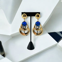 Vintage French modernist clip-on earrings with faceted blue round cabochons, layered gold and silver-tone metal crescents, and long sculptural dangles; shown from multiple angles to highlight texture, asymmetry, and mixed-metal design.
