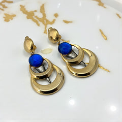 Vintage French modernist clip-on earrings with faceted blue round cabochons, layered gold and silver-tone metal crescents, and long sculptural dangles; shown from multiple angles to highlight texture, asymmetry, and mixed-metal design.