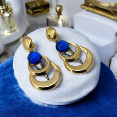Vintage French modernist clip-on earrings with faceted blue round cabochons, layered gold and silver-tone metal crescents, and long sculptural dangles; shown from multiple angles to highlight texture, asymmetry, and mixed-metal design.